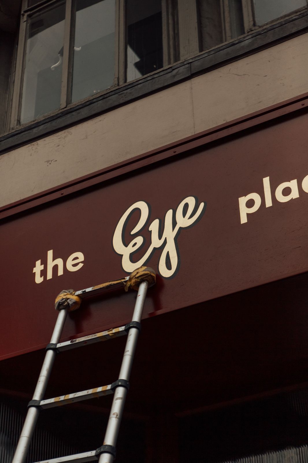 The Eye Place - branding by 93, sign-writing in gold on burgundy fascia. Ladder leading against the shop front. 